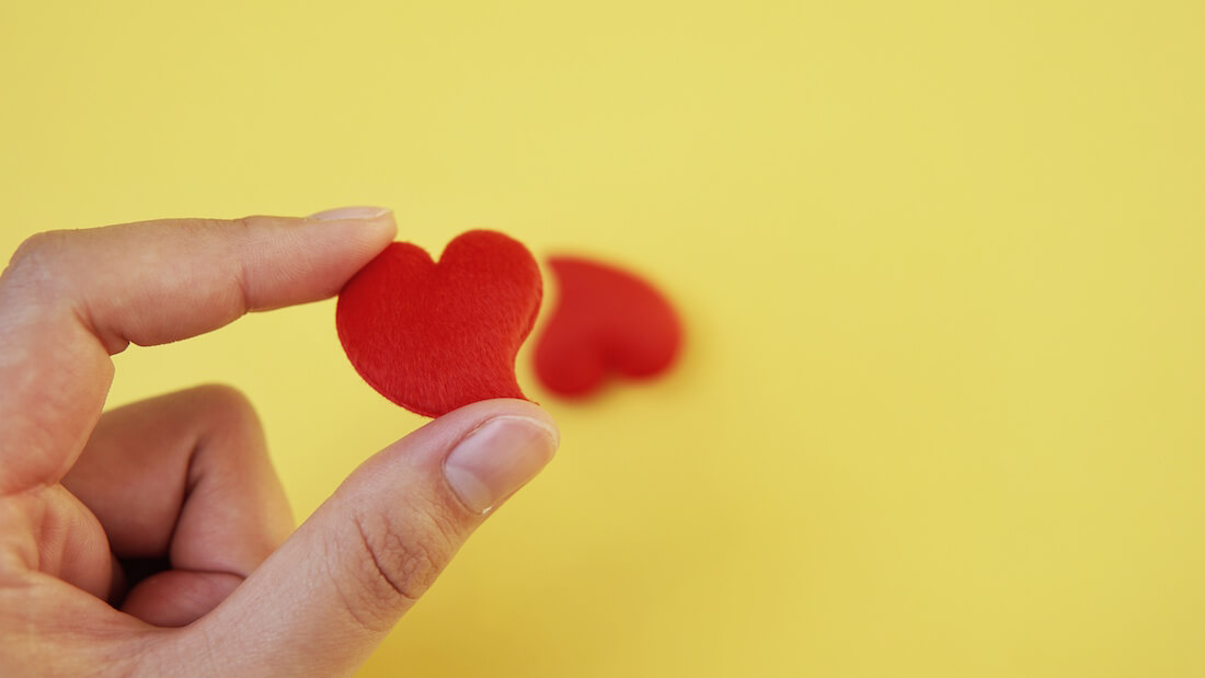 Closeup of a hand holding a tiny red heart with two fingers